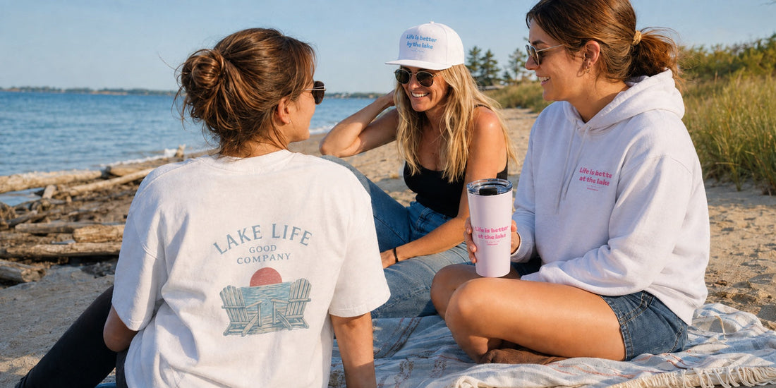 Friends relaxing on a sunny Michigan beach in Lakebound Life apparel with a pink lake tumbler